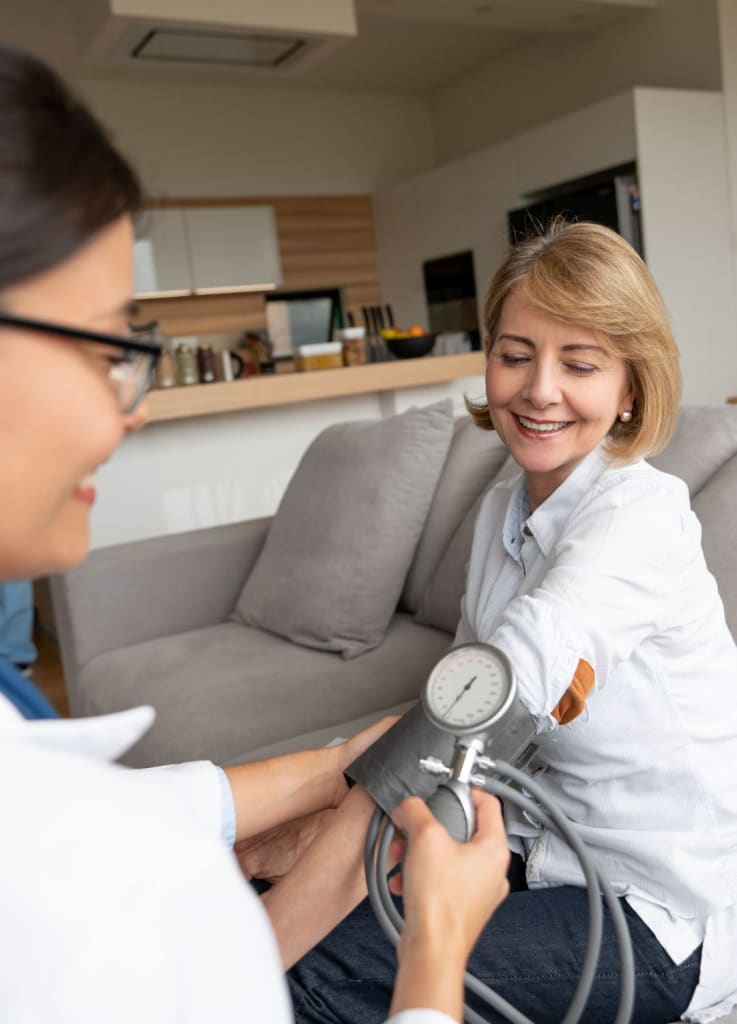A woman smiles as a concierge doctor checks her blood pressure in the comfort of her living room.